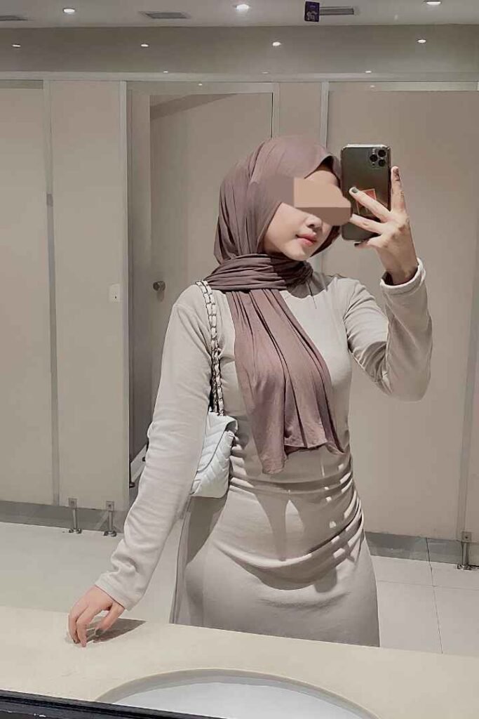 Malay Call Girl in KL, wearing a hijab, posing in a mirror selfie. Malaysia Escort services.